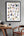 Framed Magic alphabet poster with illustrations on a wall above a wooden table and chair.