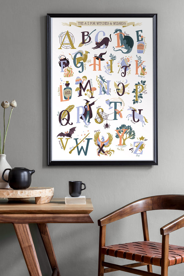 Framed Magic alphabet poster with illustrations on a wall above a wooden table and chair.