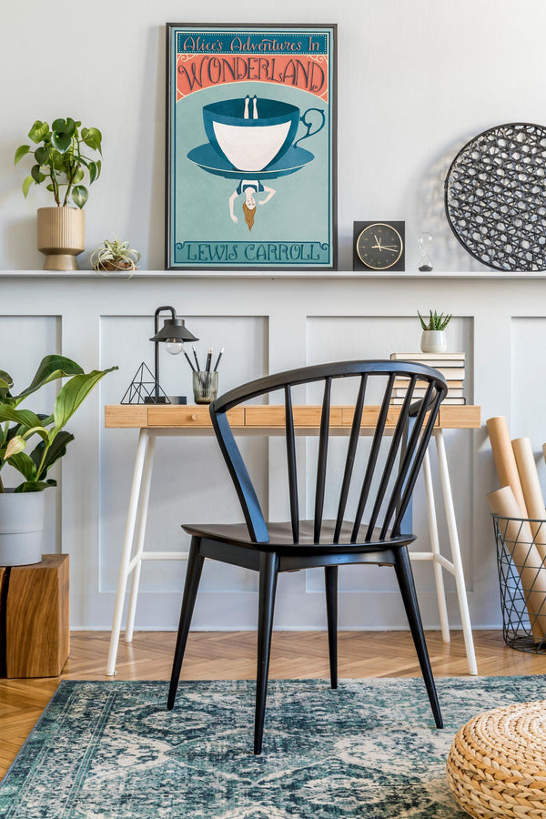 Modern home office with a black chair, wooden desk, and framed Alice In Wonderland book cover