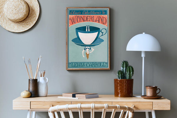 Framed Alice In Wonderland poster featuring a  teacup design on a wall above a wooden desk with a lamp and books.