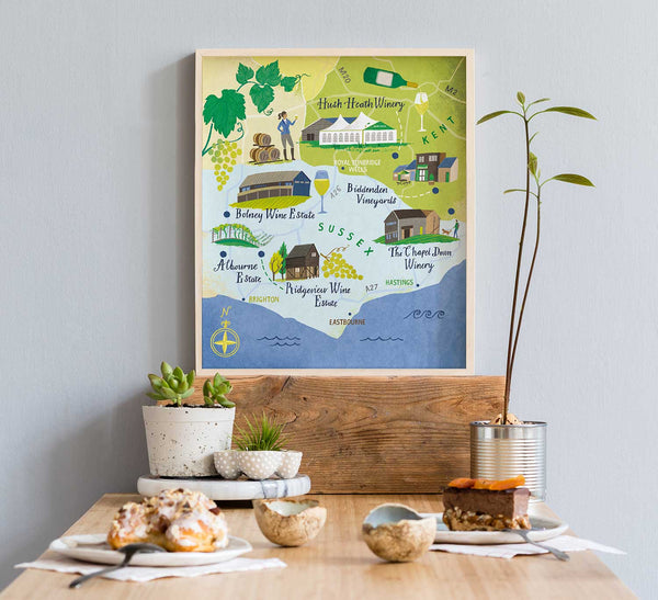 Framed map of English wine estates in Sussex and Kent on a wall above a table with food and decor.