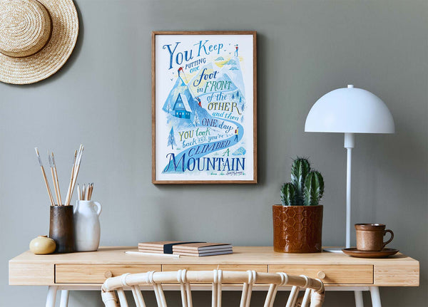 Room interior with a wooden desk, lamp, and framed motivational poster on a gray wall.