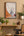 Framed artwork of  Nights at the Circus by Angela Carter on a wall above a wooden shelf with plants and decorative items.