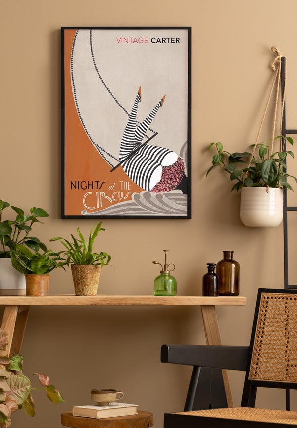 Framed artwork of  Nights at the Circus by Angela Carter on a wall above a wooden shelf with plants and decorative items.