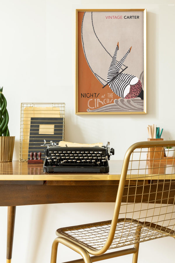 Vintage-style desk with typewriter, chair, and framed artwork of Nights at the Circus by Angela Carter on a white wall.