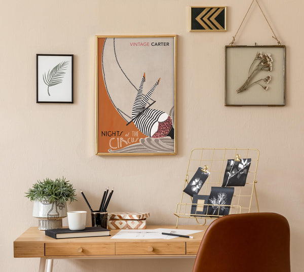 Home office with a wooden desk, chair, and wall art of Nights at the Circus by Angela Carter