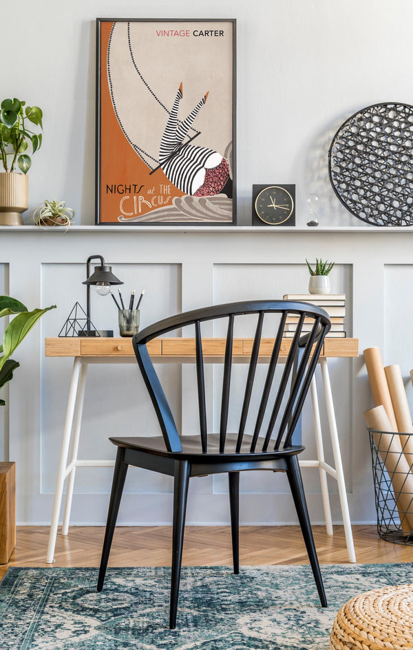 Modern interior with a black chair, wooden table, and Framed poster of Nights at the Circus by Angela Carter  'Vintage Carter' with circus-themed design 