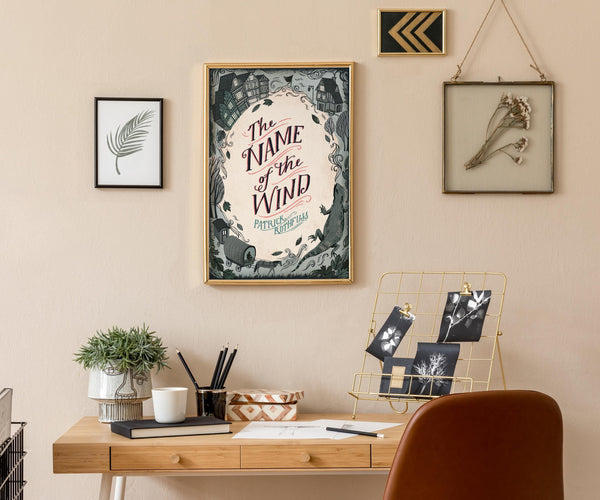 Home office with a desk, chair, and framed 'The Name of the Wind' by Patrick Rothfuss poster on the wall.