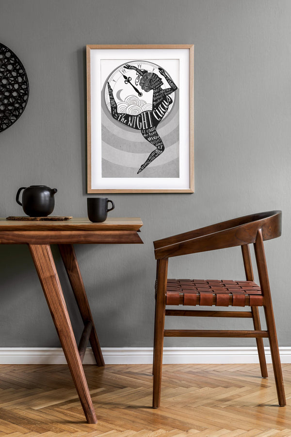 Wooden table and chair in a room with a framed black and white artwork of 'The Night Circus' on the wall.