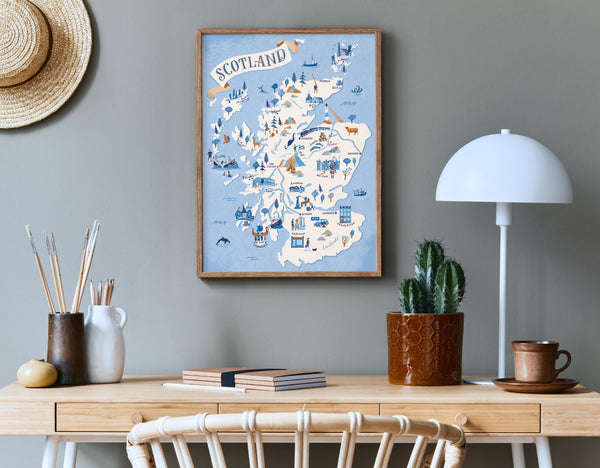Framed map of Scotland on a wall above a wooden desk with a lamp, plant, and books.